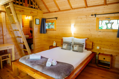Gemütliches Schlafzimmer im Baumhaus «Palombière» im Domaine EcÔtelia, Frankreich, mit natürlichen Holzwänden.