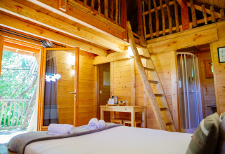 Interior of Treehouse 'Palombière' at Domaine EcÔtelia in France, featuring a loft, wooden decor and balcony.