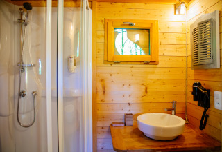 Badeværelse i træhus med bruser, håndvask og vindue på Treehouse Palombière, Domaine EcÔtelia, Frankrig.