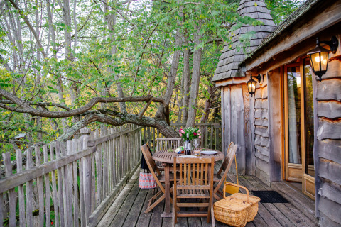 Terrazza della casa sull’albero con mobili in legno e cestino da picnic al Domaine EcÔtelia in Francia.