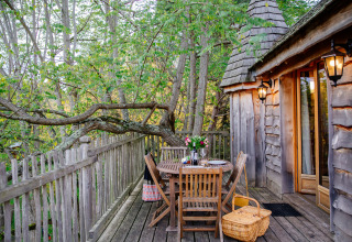Treehouse deck with wooden furniture, flowers, and picnic basket at Domaine EcÔtelia in France's forest.