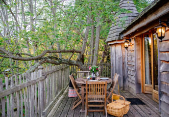 Treehouse deck with wooden furniture, flowers, and picnic basket at Domaine EcÔtelia in France's forest.