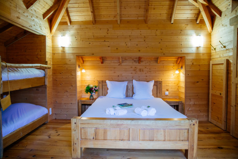Cozy treehouse bedroom at Domaine EcÔtelia, France, featuring a double bed, bunk beds, and wood interior.