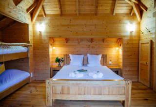 Cozy treehouse bedroom at Domaine EcÔtelia, France, featuring a double bed, bunk beds, and wood interior.