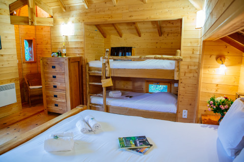 Interior view of Treehouse «Château» at Domaine EcÔtelia in France, featuring bunk beds and a double bed.