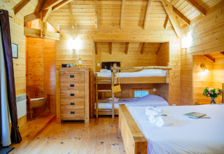 Hyggeligt træhusinteriør på Treehouse «Château» i Domaine EcÔtelia, Frankrig, med køjeseng og dobbeltseng.