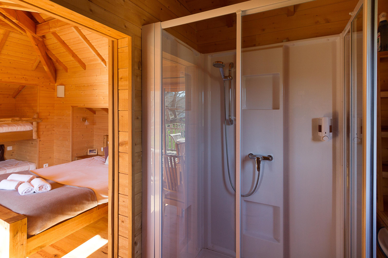 Interieur van een boomhut bij Domaine EcÔtelia in Frankrijk met bed en doucheruimte met houten muren.