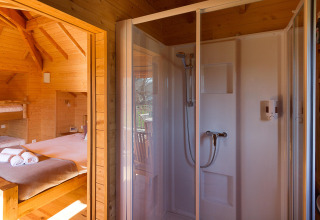 Interior of a treehouse at Domaine EcÔtelia in France showing a bed and shower cabin with wooden walls.