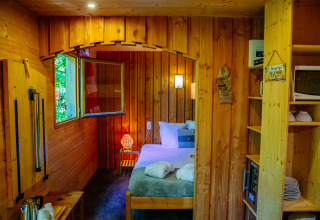 Cozy lodge interior with a double bed, wood paneling, open window, and a kitchenette with microwave.