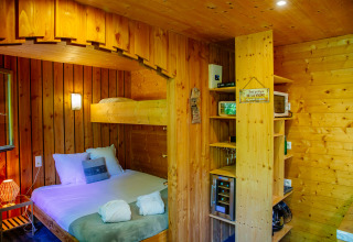 Wood-paneled lodge room featuring a double bed, bunk bed, shelves, minibar, and cozy lighting.