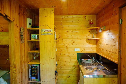 Cozy wood-paneled kitchenette in a lodge, featuring a sink, stove, wine fridge, shelves and decor.