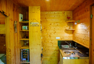 Cozy wood-paneled kitchenette in a lodge, featuring a sink, stove, wine fridge, shelves and decor.