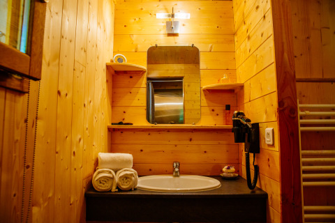 Cozy wooden bathroom at Oenolodge, Domaine EcÔtelia, France featuring a sink, mirror, towels, and shelves.