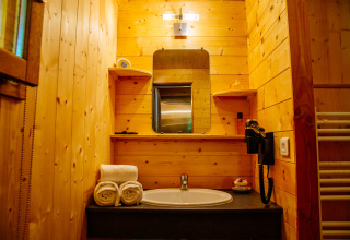 Cozy wooden bathroom at Oenolodge, Domaine EcÔtelia, France featuring a sink, mirror, towels, and shelves.