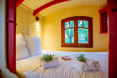 Lit douillet dans la roulotte Gypsy au Domaine EcÔtelia en France, avec vue sur les arbres par la fenêtre.