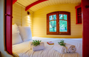 Cozy bed inside the Gypsy wagon cabin at Domaine EcÔtelia, France, with window view of trees and garden.