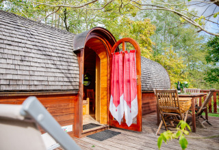Caravana de madera con puerta abierta y cortina roja en terraza, comedor exterior en Domaine EcÔtelia, Francia.