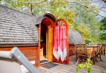 Caravana de madera con puerta abierta y cortina roja en terraza, comedor exterior en Domaine EcÔtelia, Francia.