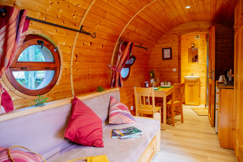 Gemütliche Holzhütte mit runden Fenstern, Essbereich, Sofa mit roten Kissen und hellem Holzinterieur.