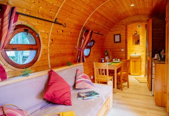 Gemütliche Holzhütte mit runden Fenstern, Essbereich, Sofa mit roten Kissen und hellem Holzinterieur.