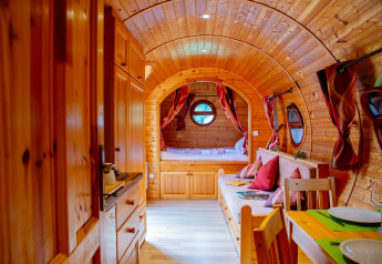 Interior de una acogedora cabaña de madera con techo curvo, mesa de comedor, sofá y cama al fondo.
