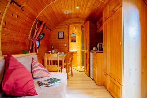 Gemütliches Holzhütten-Interieur mit Sofa, Esstisch, Küche und natürlichem Licht, einladende Atmosphäre.