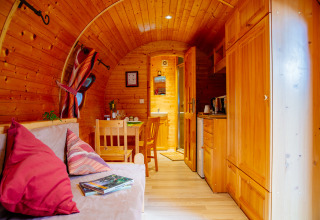 Gemütliches Holzhütten-Interieur mit Sofa, Esstisch, Küche und natürlichem Licht, einladende Atmosphäre.