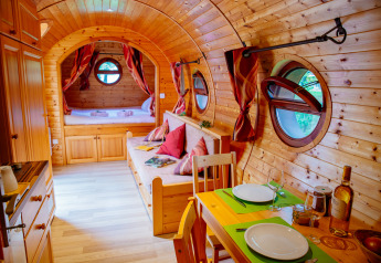 Gemütliche Holzhütte mit runden Fenstern, Esstisch, Sofa und Bett im Hintergrund, warm dekoriert.