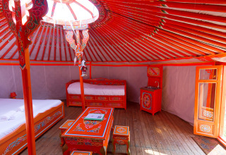 Interior de una yurta tradicional mongola en Domaine EcÔtelia, Francia, con colorida decoración y camas.