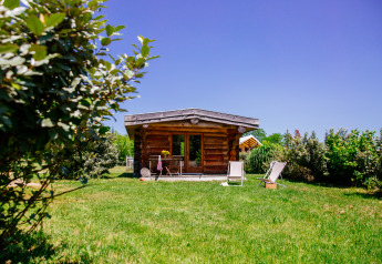 Blockhütte im Grünen, umgeben von Bäumen, mit Liegestühlen vor Domaine EcÔtelia in Frankreich.
