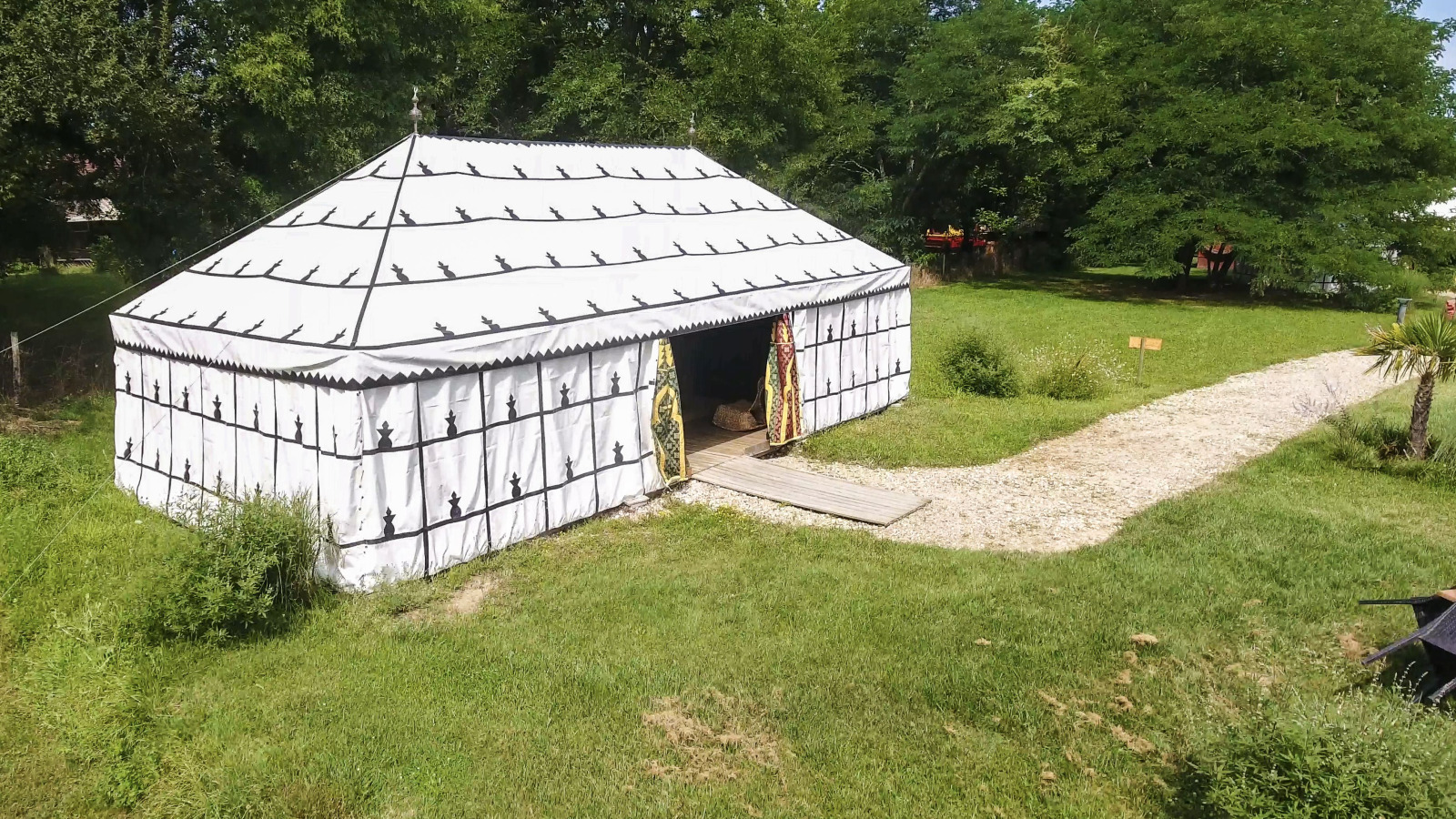De safari-tent 'Caïdale' bij Domaine EcÔtelia in Frankrijk, omgeven door gras, bomen en een grindpad.