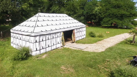 La tienda safari 'Caïdale' en Domaine EcÔtelia, Francia, rodeada de césped, árboles y un camino de piedras.