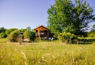 Tenda safari al Domaine EcÔtelia in Francia, immersa nel verde tra prati e alberi in una giornata soleggiata.