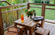 Tavolo in legno con fiori, vino, cestino da picnic e acquerelli sulla veranda della tenda Safari, Domaine EcÔtelia.
