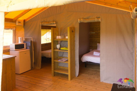 Interno di una tenda safari con due camere da letto, angolo cottura e pavimento in legno a Domaine EcÔtelia, Francia.