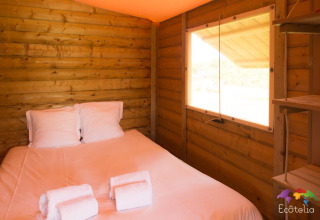 Vista interna di una tenda Safari al Domaine EcÔtelia in Francia con letto matrimoniale e pareti in legno.