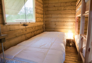 Acogedora habitación de madera con literas y ventana en la tienda 'safari' de Domaine EcÔtelia en Francia.
