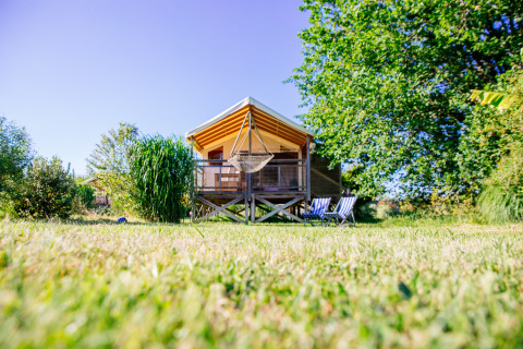 Safari-Zelt im Domaine EcÔtelia in Frankreich, mit Veranda, Hängesessel und Gartenstühlen.