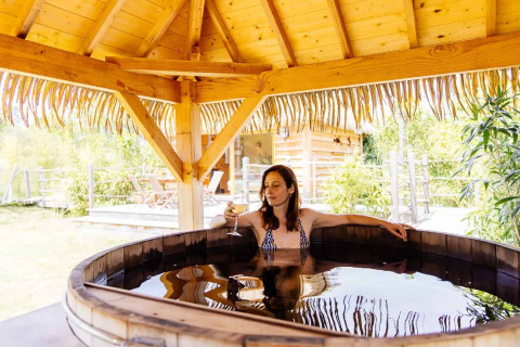 Woman relaxing in a wooden hot tub under thatched roof at Indonesian hut, Domaine EcÔtelia, France.