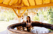 Mujer relajándose en una tina de madera bajo techo de paja en Indonesian hut, Domaine EcÔtelia, Francia.