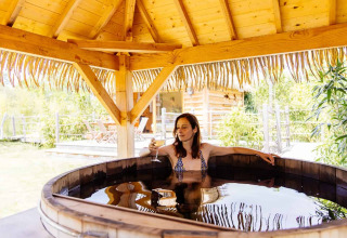Mujer relajándose en una tina de madera bajo techo de paja en Indonesian hut, Domaine EcÔtelia, Francia.