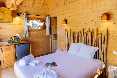 Cozy bedroom with wooden walls and rustic decor in an Indonesian hut at Domaine EcÔtelia, France.