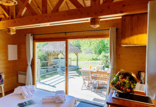 Vista dall’interno di una capanna indonesiana a Domaine EcÔtelia, Francia, con terrazza e tavolo all’aperto.
