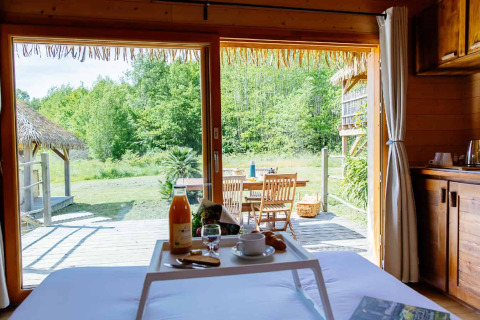 Udsigt fra sengen på et indonesisk hus ved Domaine EcÔtelia i Frankrig, med morgenmad og træterrasse.