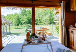 Vue du lit dans une hutte indonésienne au Domaine EcÔtelia, France, avec petit-déjeuner et terrasse boisée.