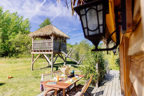 Buitenaanzicht van een Indonesische hut met rieten dak en eettafel bij Domaine EcÔtelia in Frankrijk.