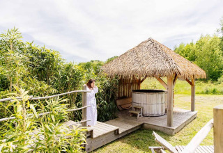 Mujer con bata junto a cabaña indonesia con jacuzzi en Domaine EcÔtelia, Francia, rodeada de naturaleza.
