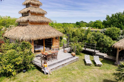 Indonesisk hytte med stråtag og træterrasse på Domaine EcÔtelia i Frankrig omgivet af grøn natur.