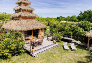 Indonesische hut met rieten dak bij Domaine EcÔtelia in Frankrijk, omgeven door groen en houten terras.