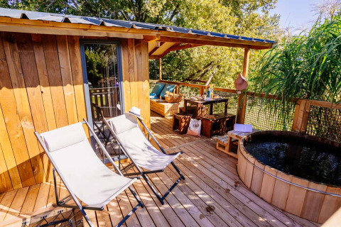 Sonnige Holzterrasse bei Océania Lodge, Domaine EcÔtelia, mit Liegestühlen, Hot Tub und gemütlicher Sitzecke.